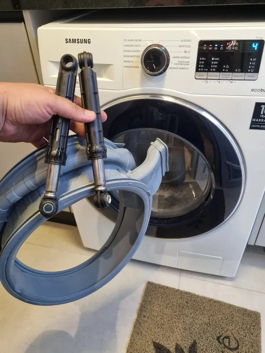 Técnico segurando dois amortecedores e o fole retirados de uma lava e seca Samsung