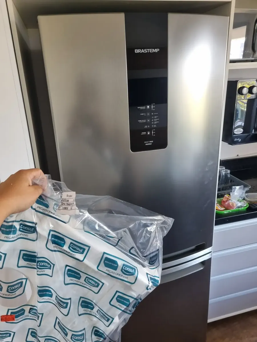 Técnico segurando uma peça original Whirlpool em frente a uma Brastemp Frost Free Inverse inox