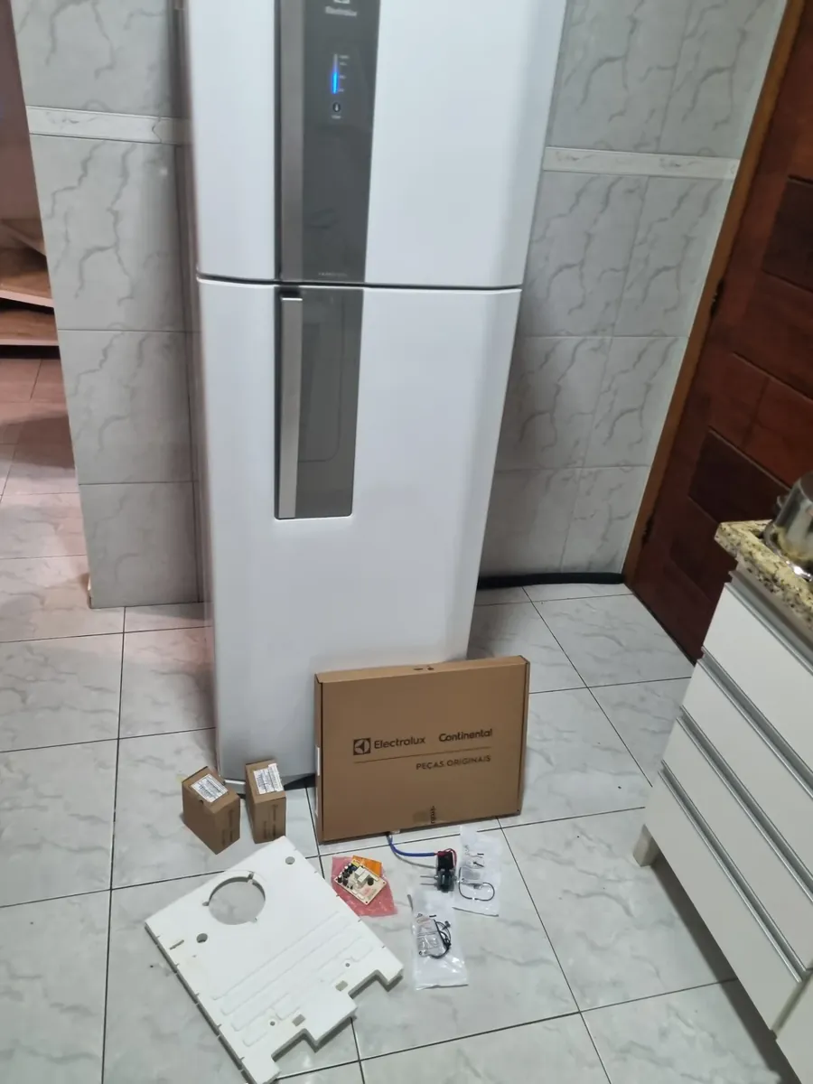 Placa eletrônica e peças originais Electrolux separadas no chão, antes da instalação na geladeira